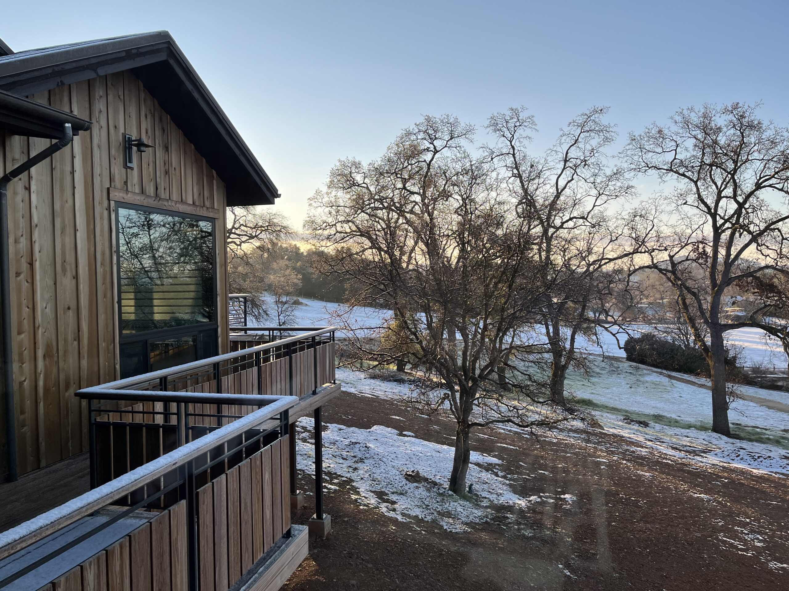 Wooden building with a balcony overlooking a frosty landscape with sparse snow and leafless trees under a clear sky.
